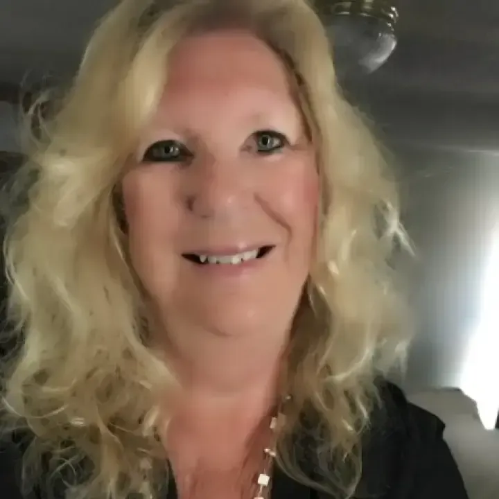 Smiling blonde woman indoors, with soft lighting and a car interior in the background