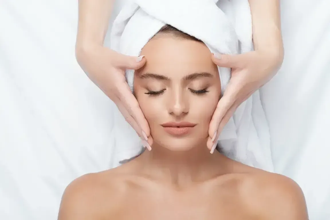 Woman receiving a facial massage with white towels, eyes closed, on a spa bed