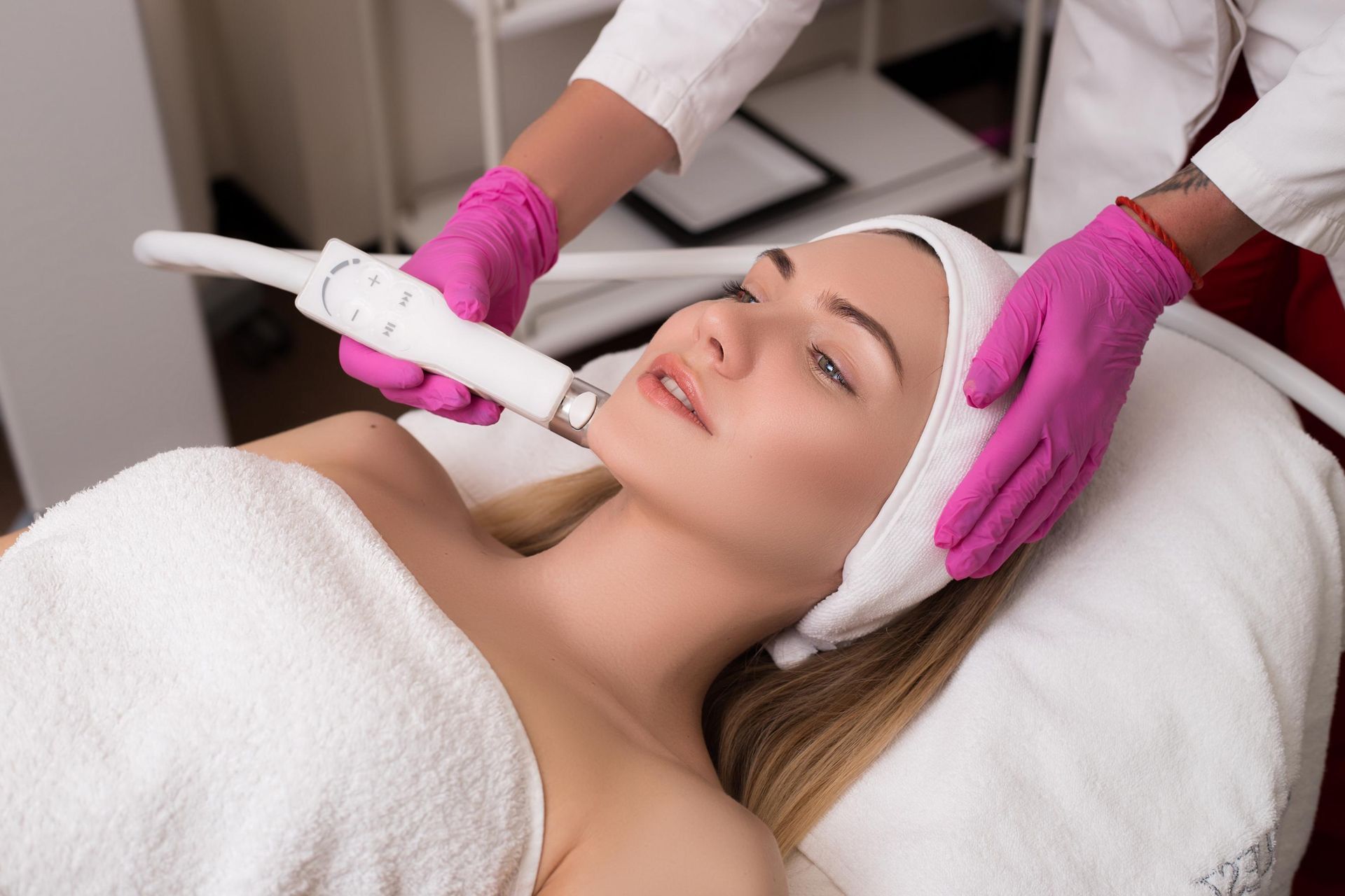 Facial treatment with technician using a handheld device on a woman in a spa, wearing pink gloves