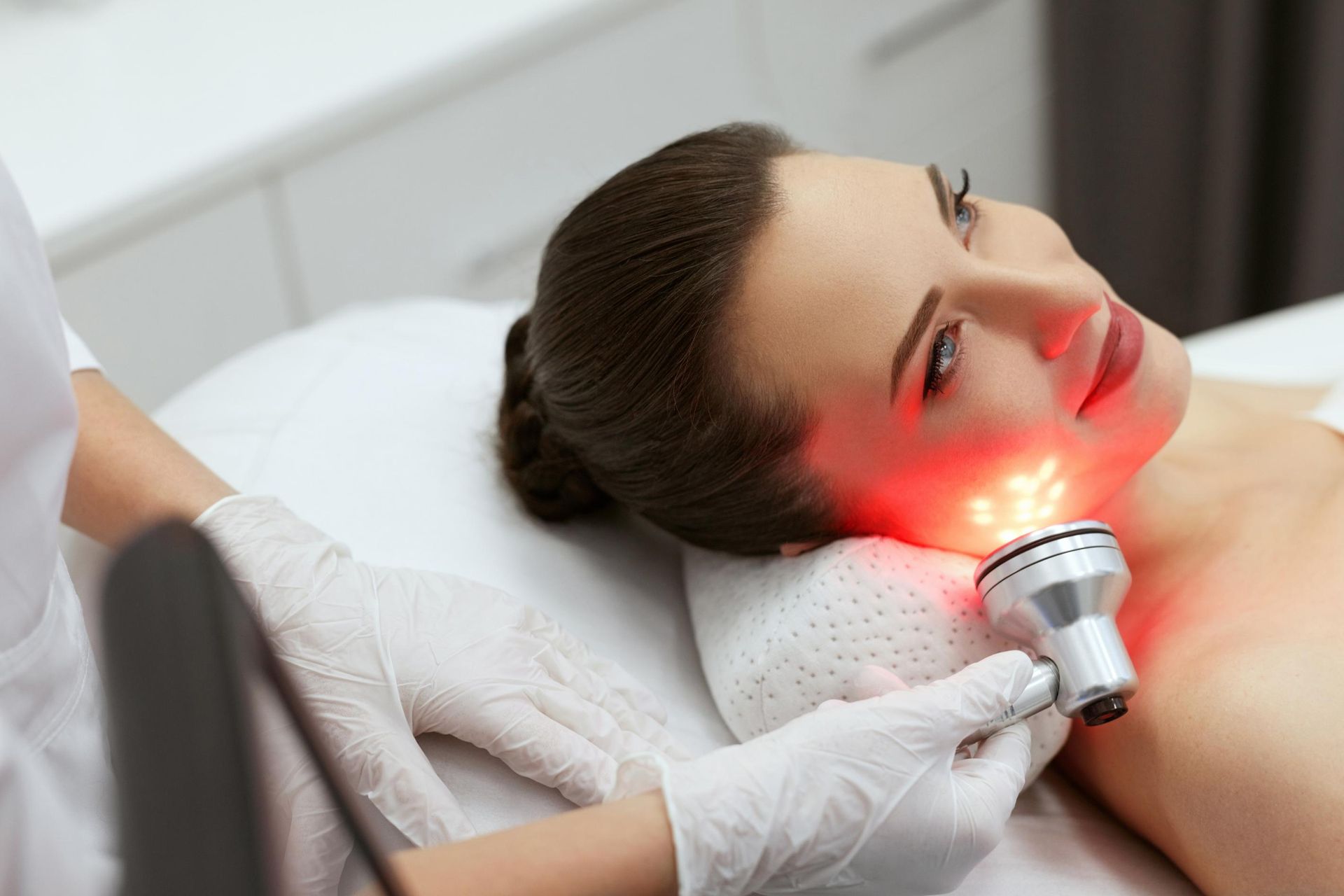 Woman receiving a red light facial treatment while lying on a spa bed