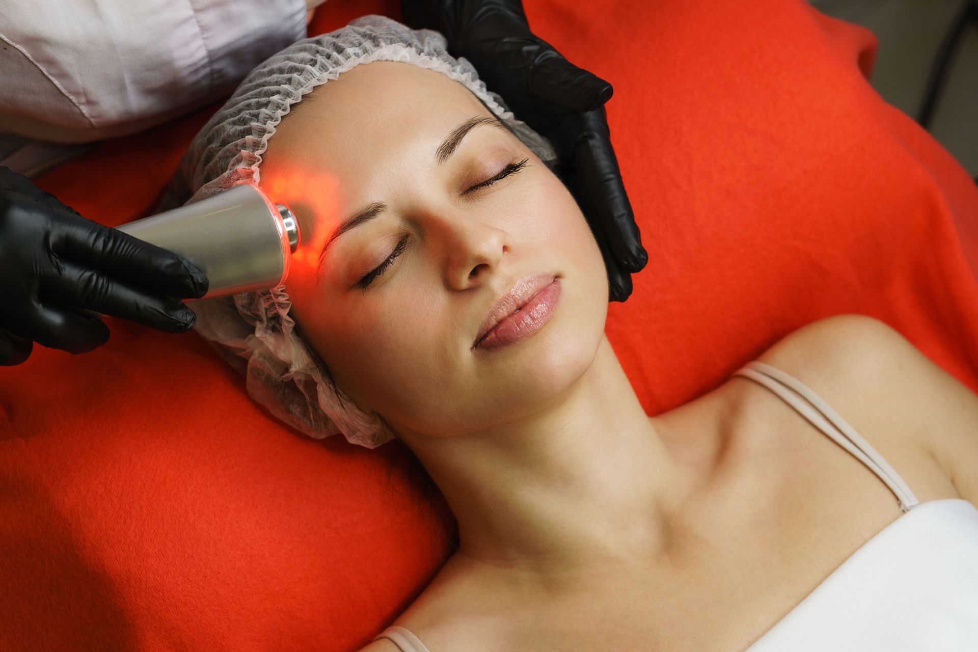 Woman receiving a facial treatment with a glowing device while lying on a red spa bed