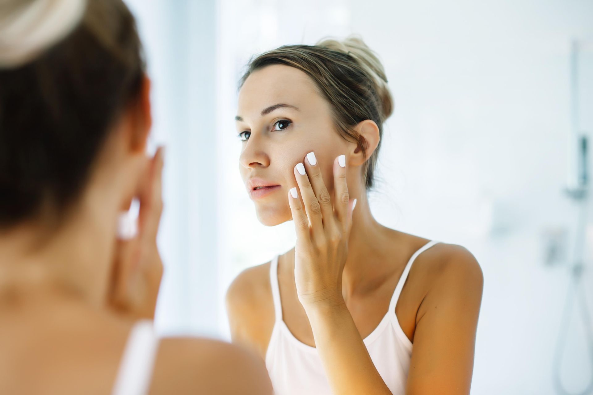 Woman applying cream to her face in a bathroom mirror