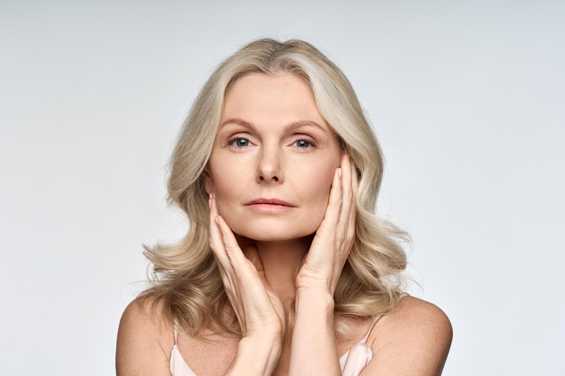 Portrait of a blonde woman touching her face against a light gray background