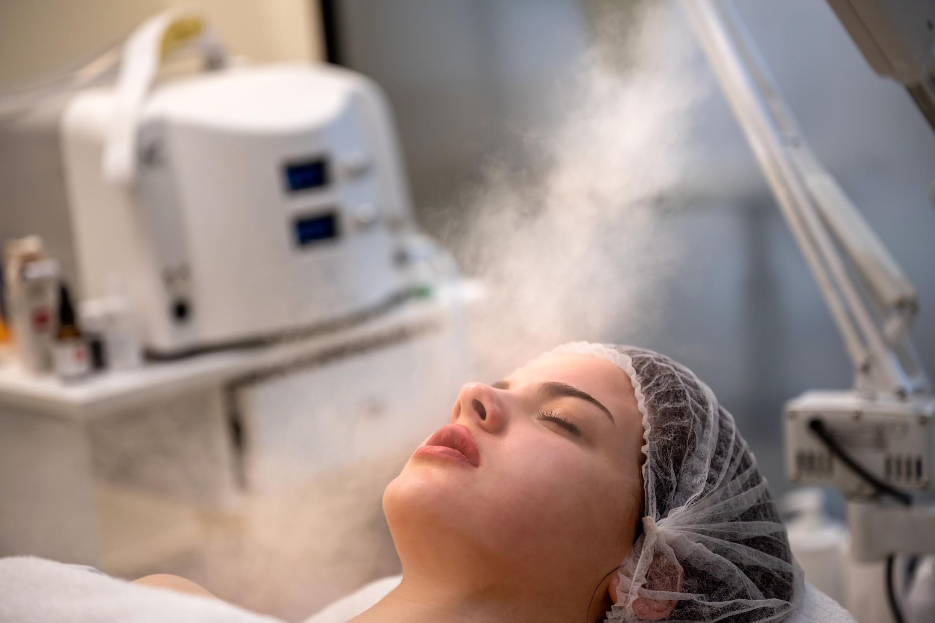 Person with closed eyes receiving a facial steam treatment in a spa-like setting