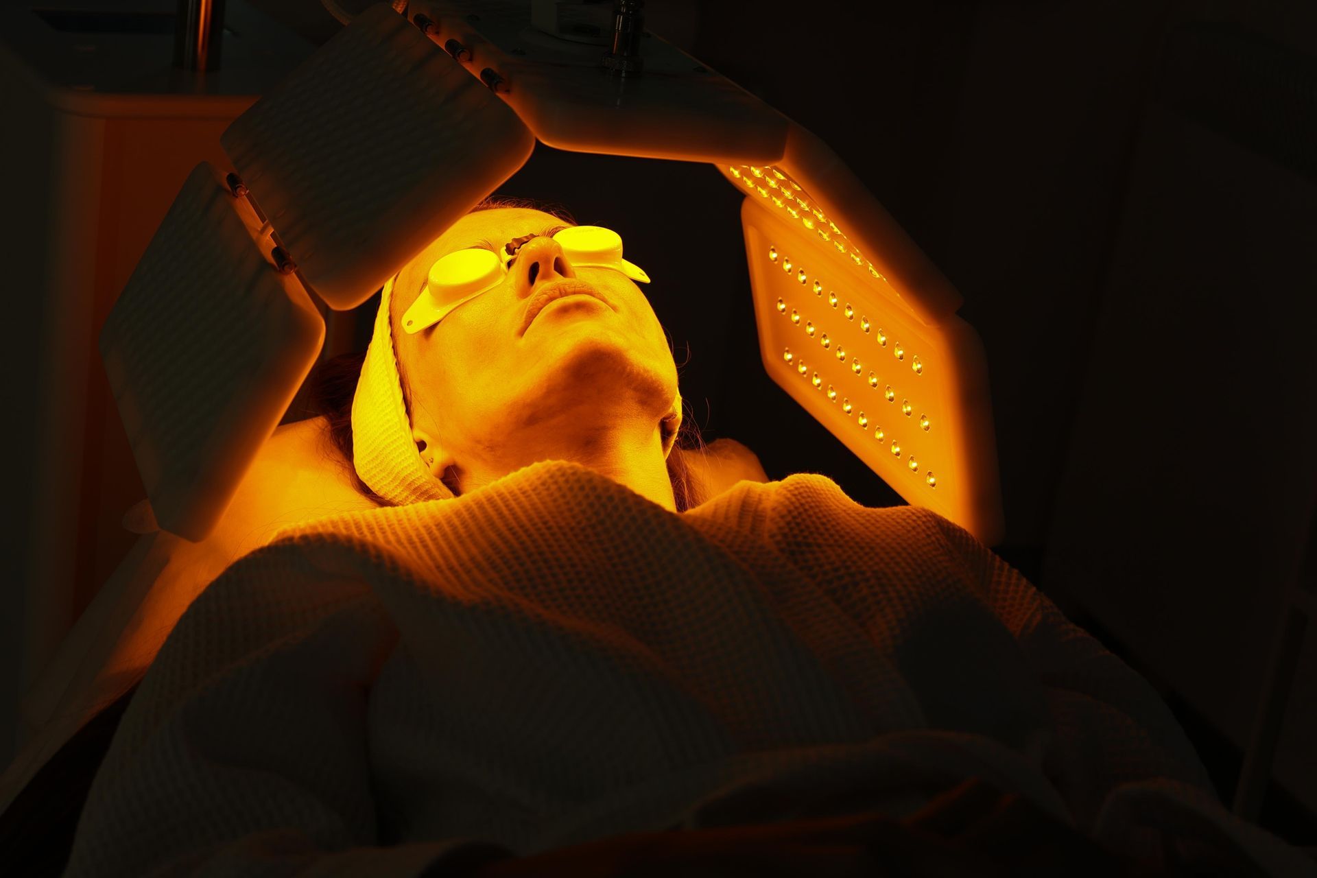 Person lying under an orange-lit panel in a dark chamber, wearing glasses and looking upward
