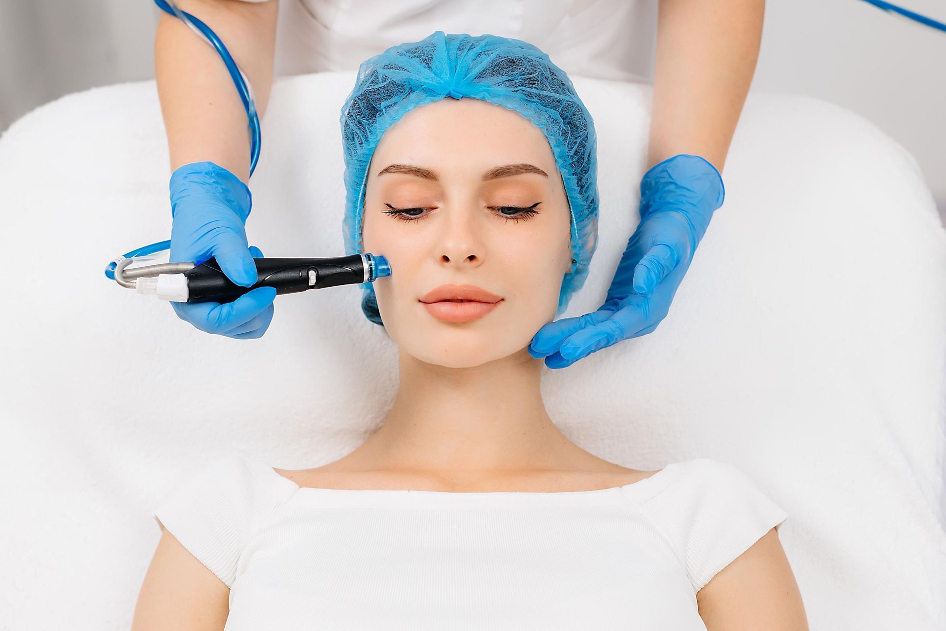 Cosmetic procedure in progress as gloved hands use a facial injection on a woman with blue hair net