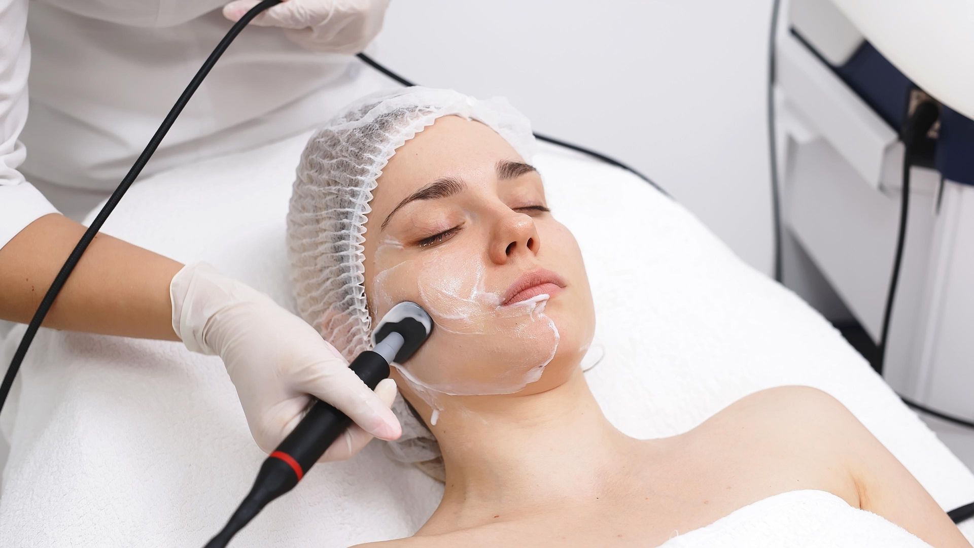 Facial treatment with a handheld device on a client lying on a spa bed