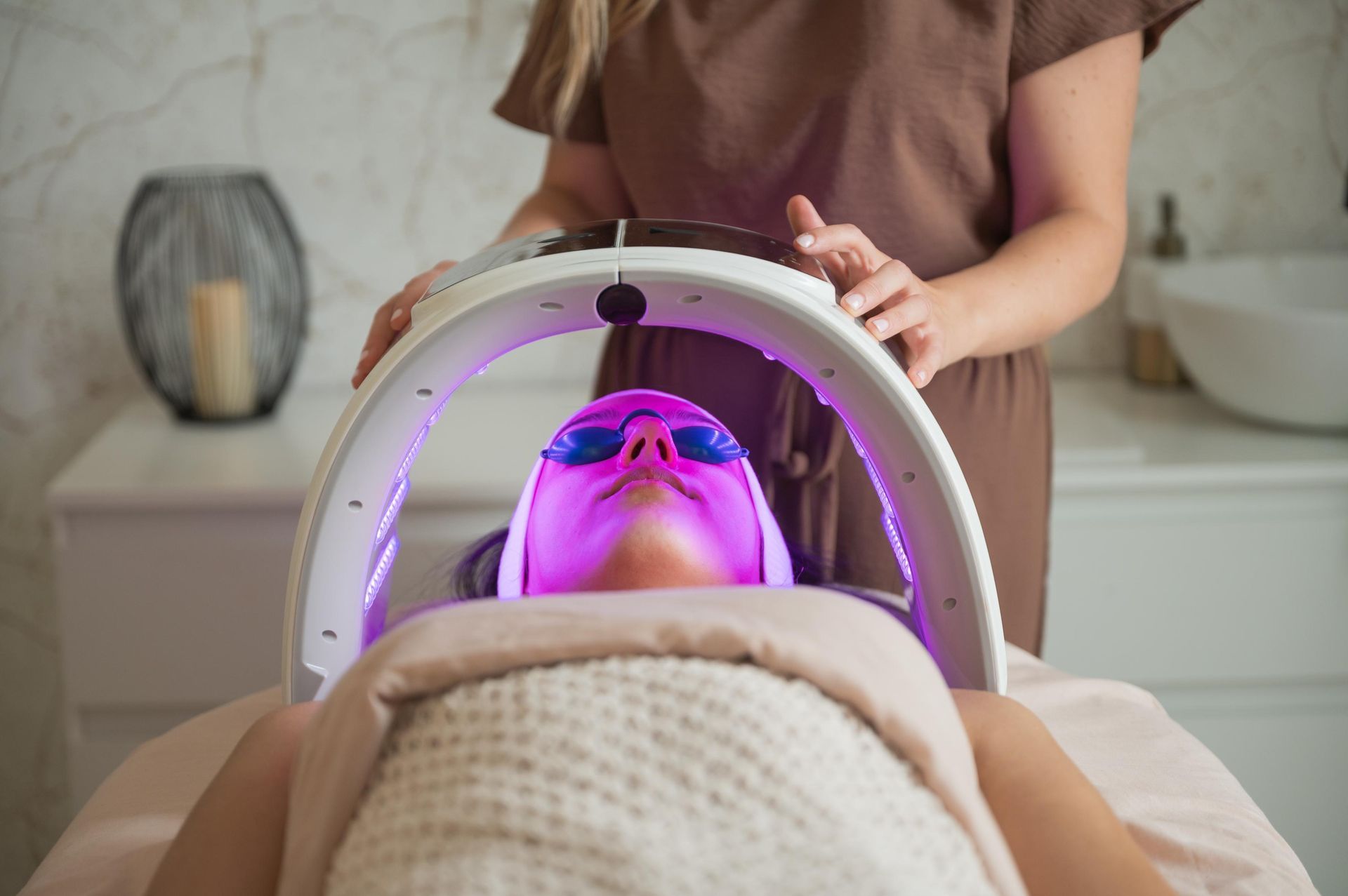 Person receiving a pink LED light facial treatment in a spa room