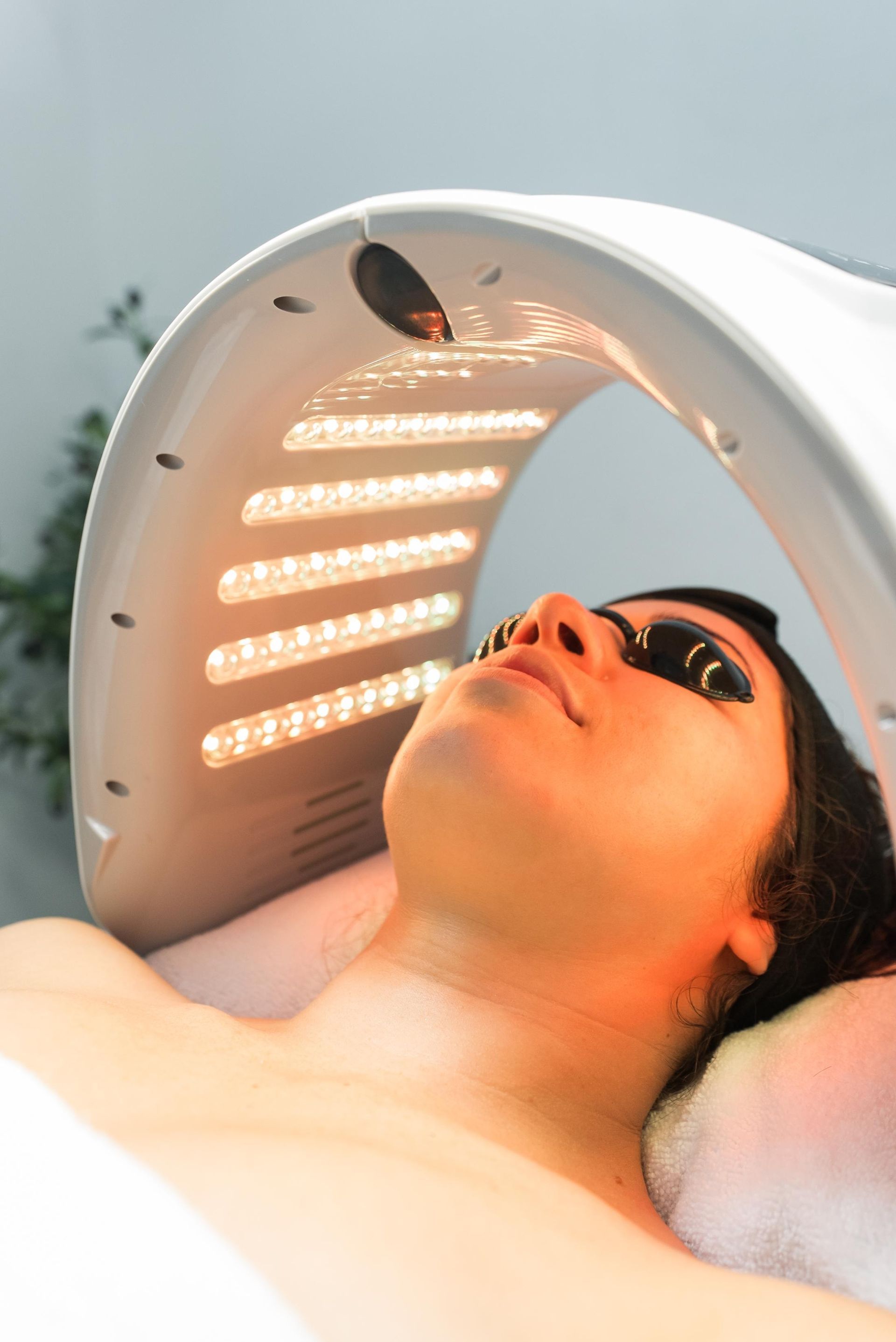 Person lying under a red light therapy panel during a facial treatment
