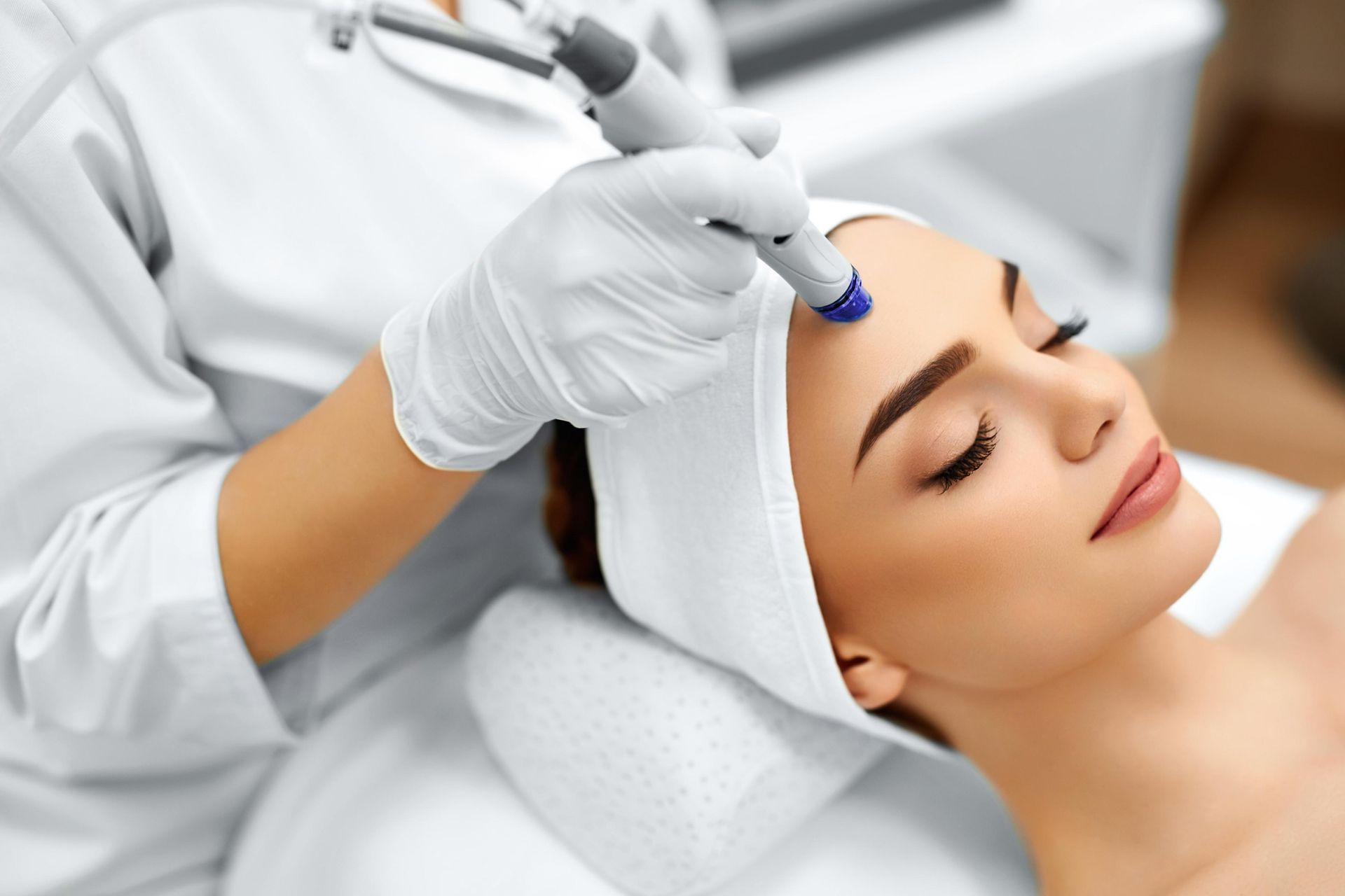 A clinician applies a handheld device to a woman’s forehead during a facial treatment.