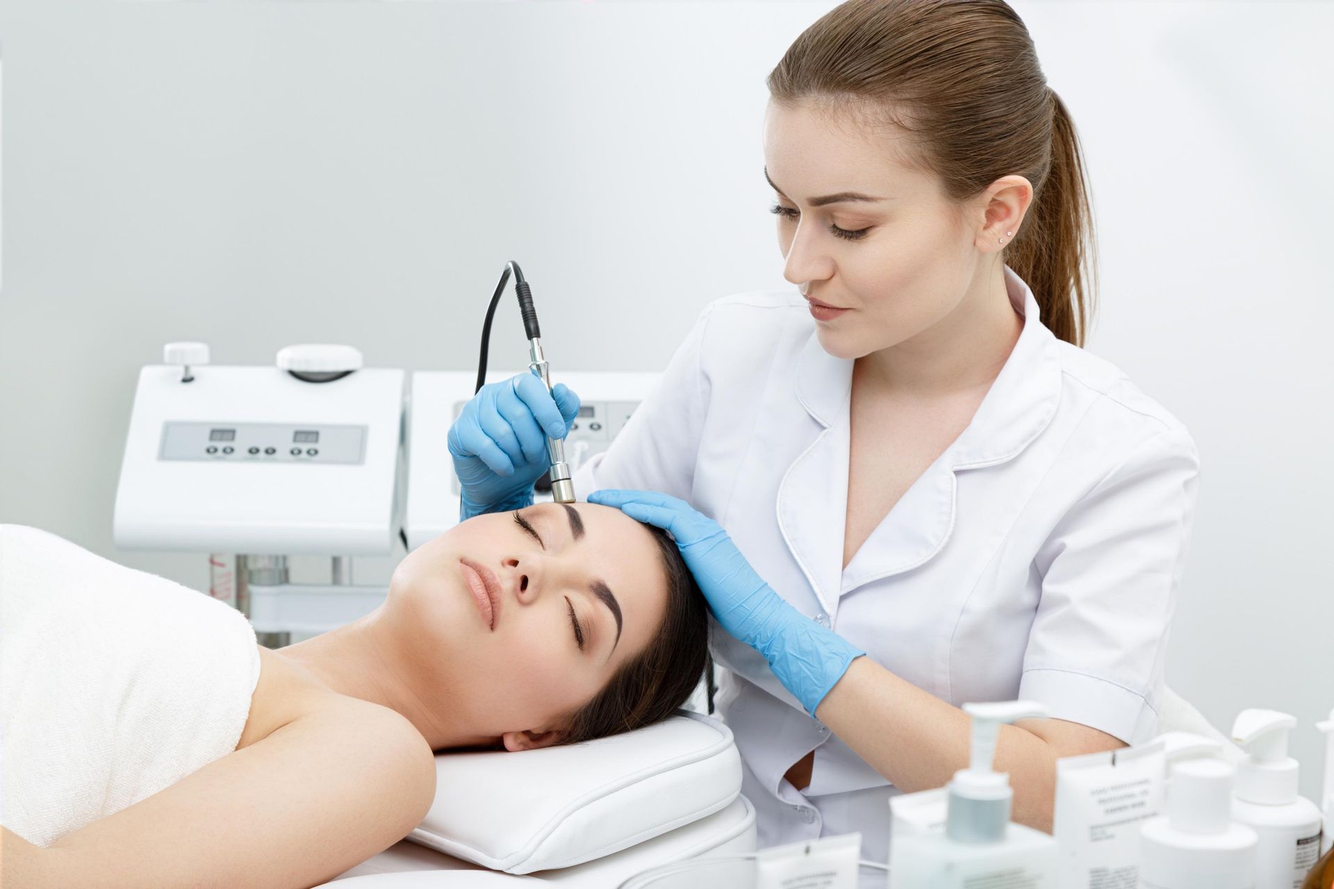 Aesthetic treatment in a clinic, with a practitioner applying a procedure to a patient lying on a bed.