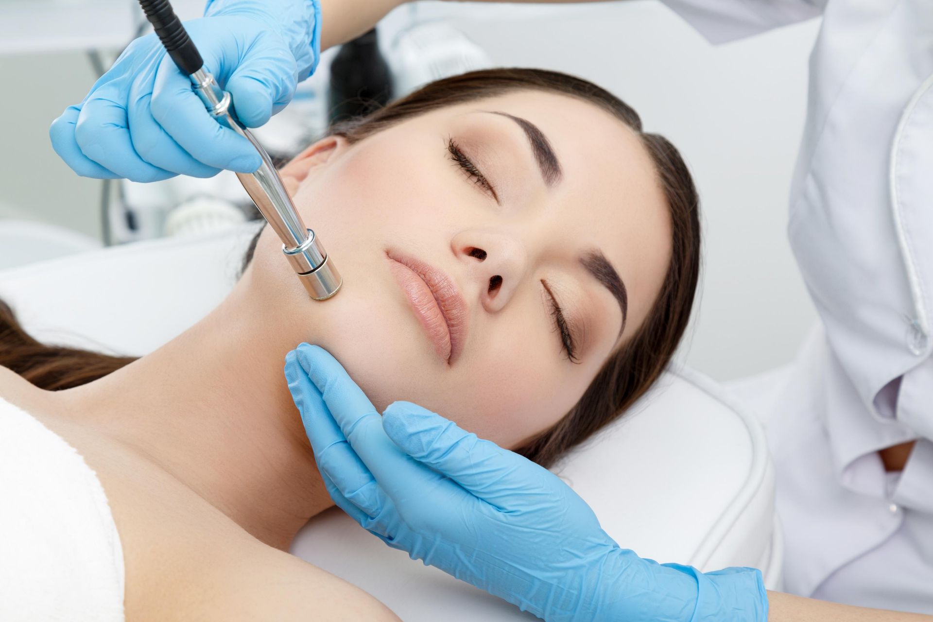 Cosmetic facial treatment with a gloved practitioner using a handheld device on a relaxed patient