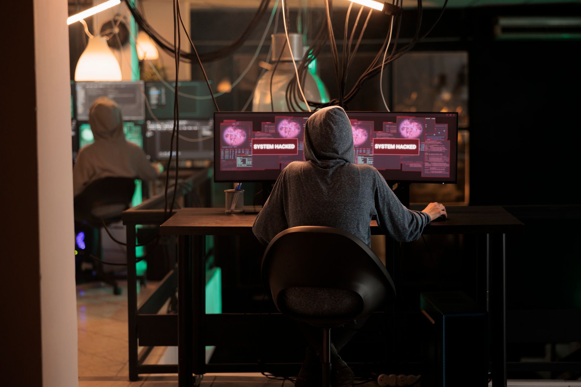 Um hacker sentado em uma mesa em frente a dois monitores de computador