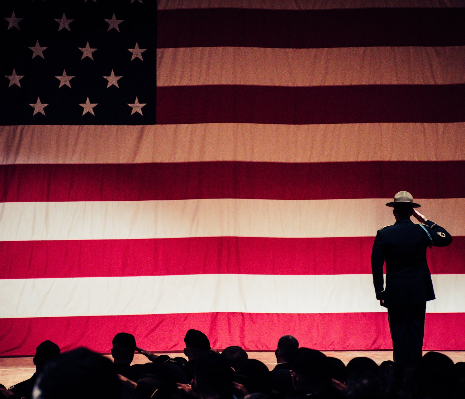 Soldier salutes large American flag; group of people salute in the foreground in Spring Lake, NC.
