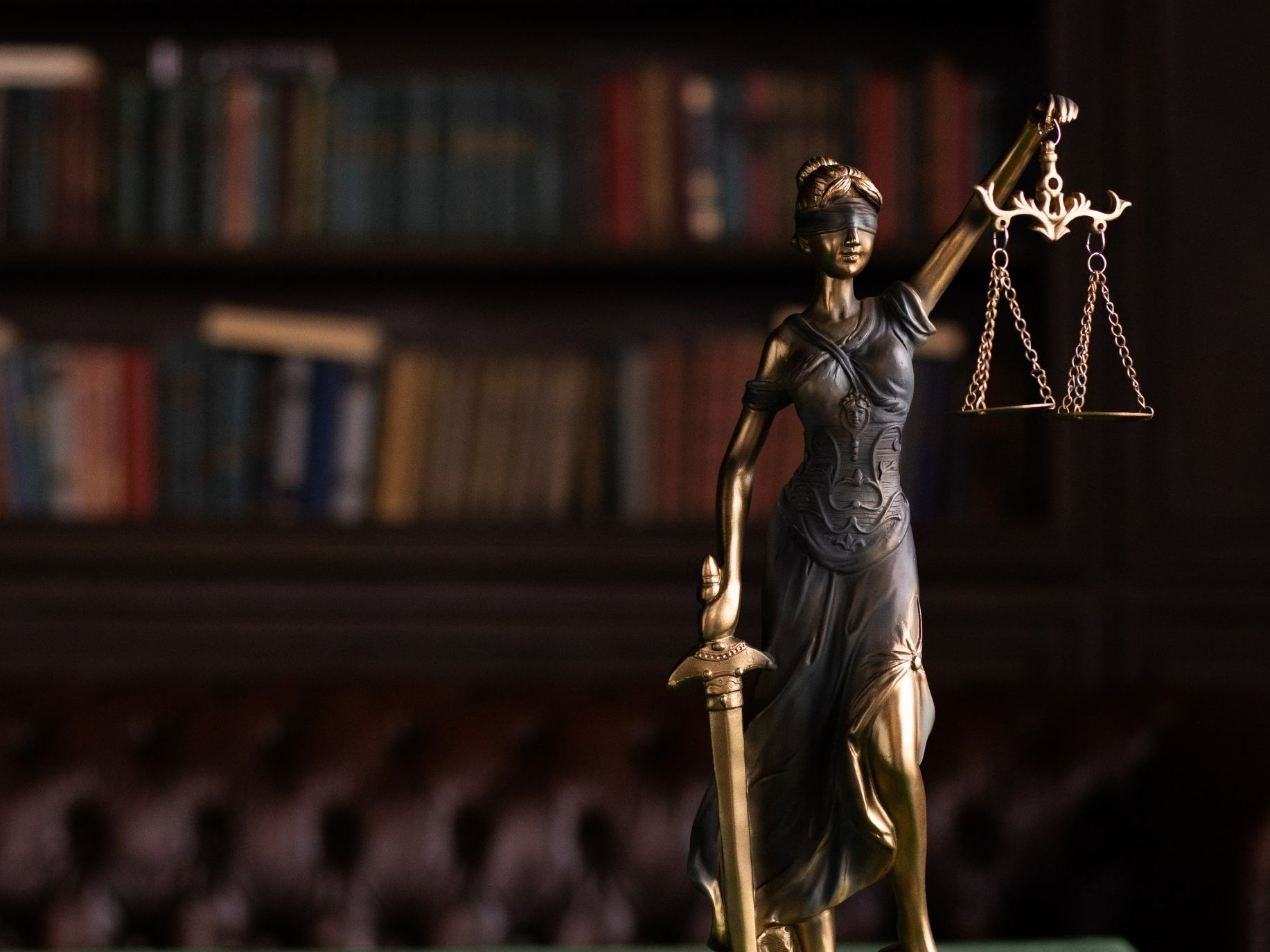 Statue of Lady Justice holding scales and sword, with a library in the background in Spring Lake, NC.