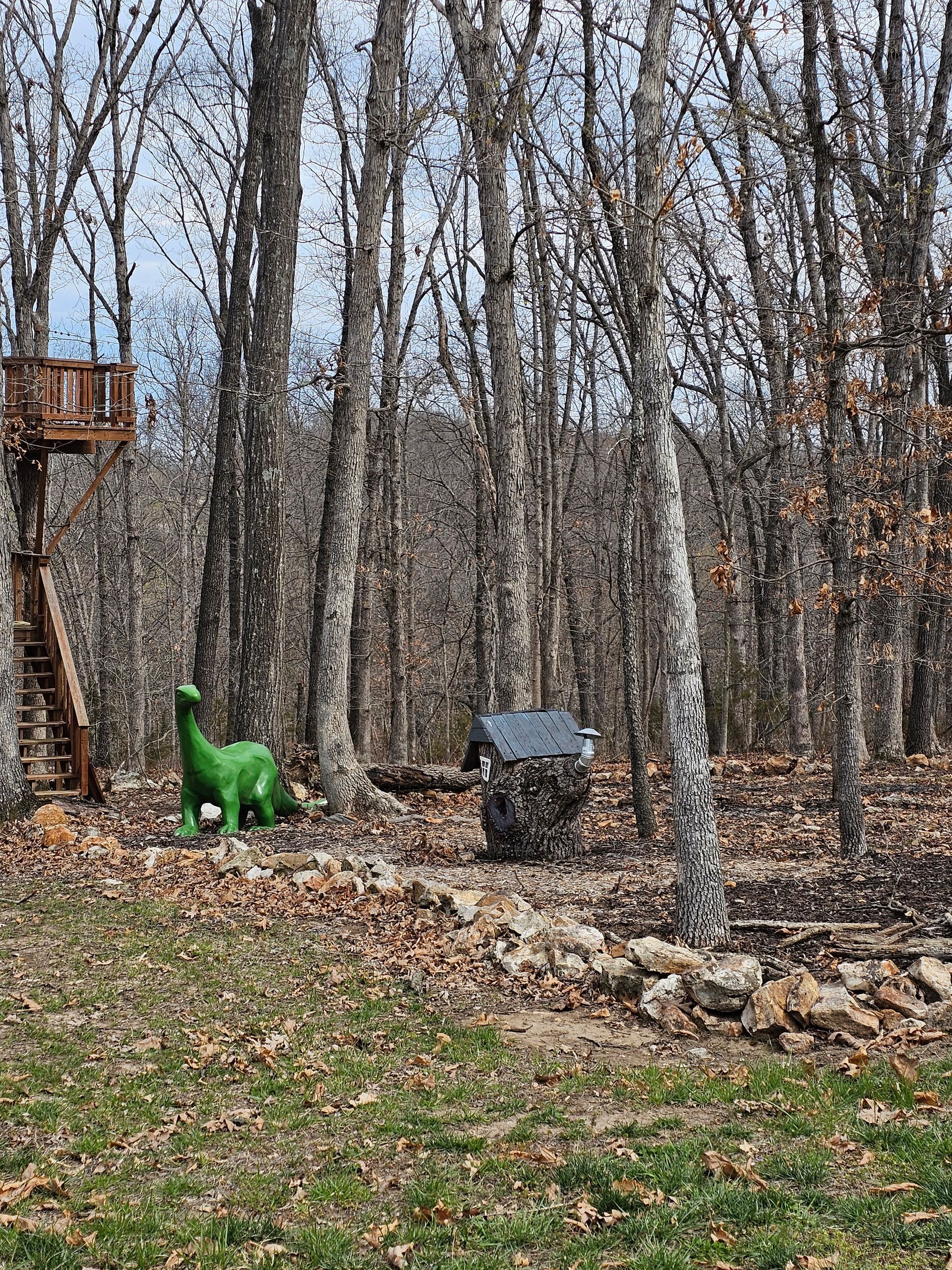Green dinosaur toy near a stump in a leaf-covered woodland clearing