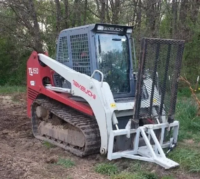 Red and white Bobcat tracked skid steer with grapple attachment parked on dirt in a wooded area