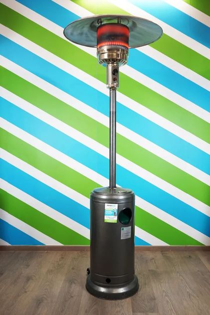 Riscaldatore da esterno per patio con asta argentata e base nera, su uno sfondo di muro a strisce blu, verdi e bianche.