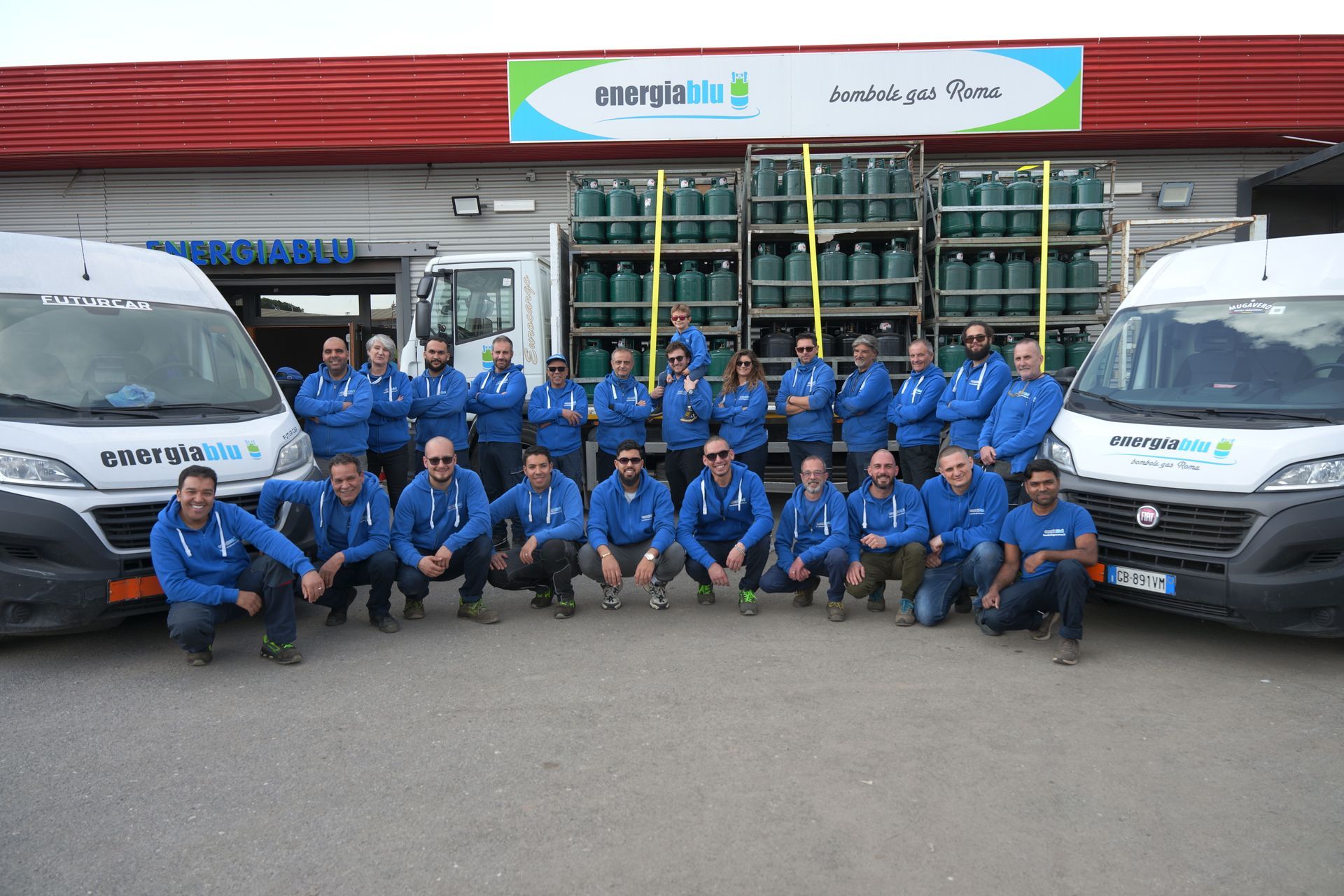 Una squadra in uniforme blu posa davanti a camion e casse impilate nell'area di carico di un magazzino.