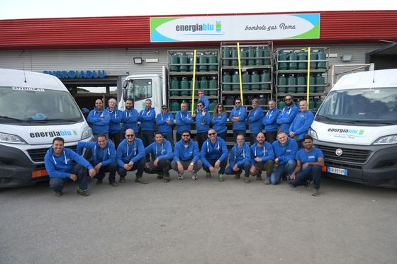 Una squadra in uniforme blu posa davanti a camion e casse impilate nell'area di carico di un magazzino.