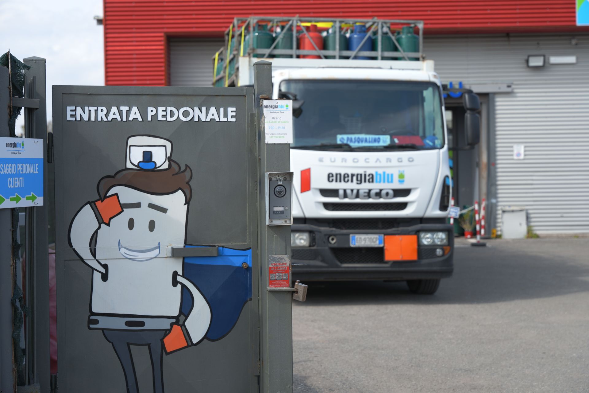 Un operaio apre un cancello blu accanto a un camion all'ingresso industriale con la scritta