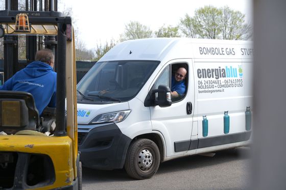 Un carrello elevatore si trova vicino a un furgone bianco per le consegne con il logo aziendale in un parcheggio all'aperto.