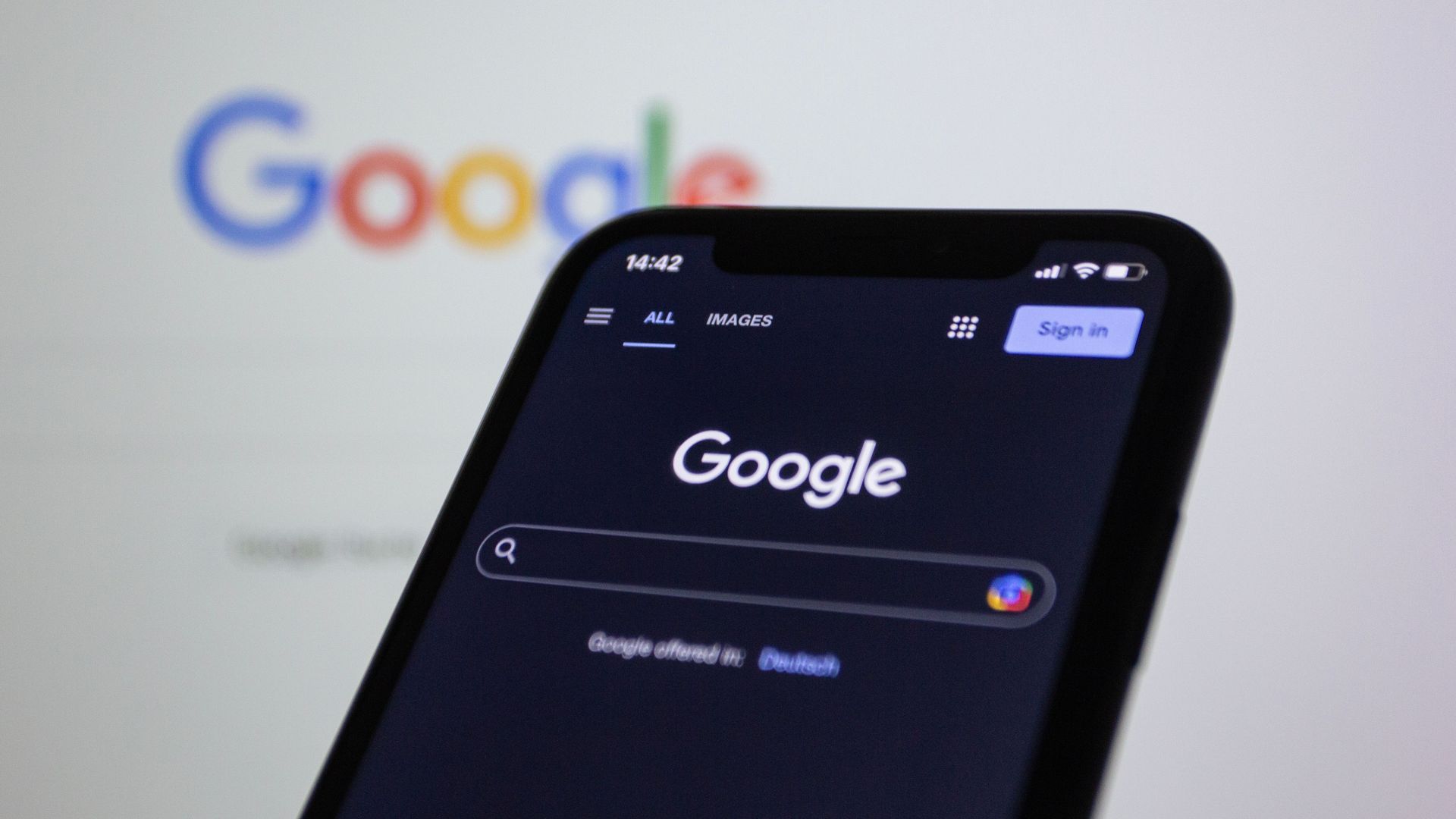 Smartphone showing Google search page in dark mode, with blurred Google logo in the background