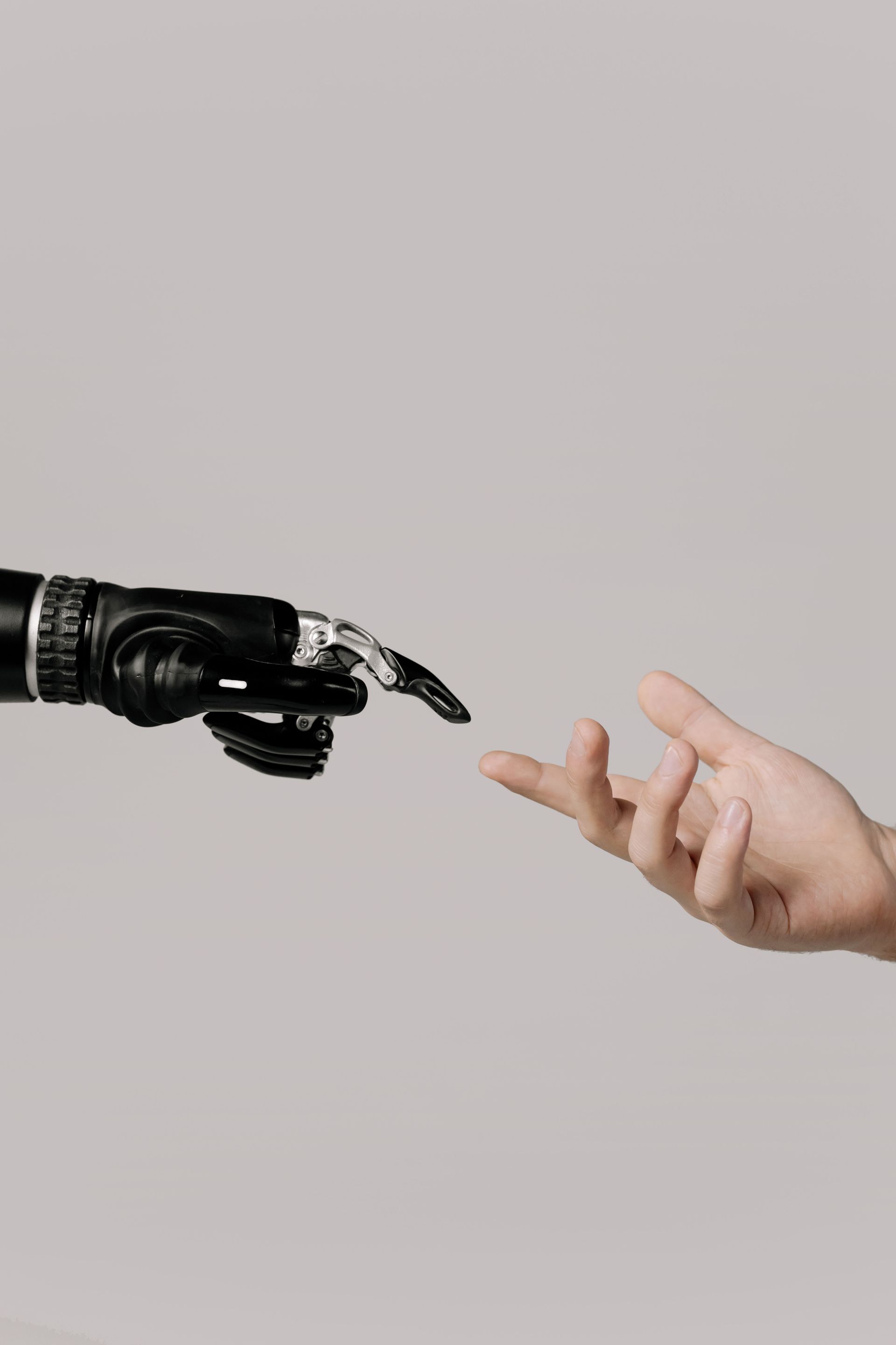 Robotic black hand reaching toward a human hand against a light gray background
