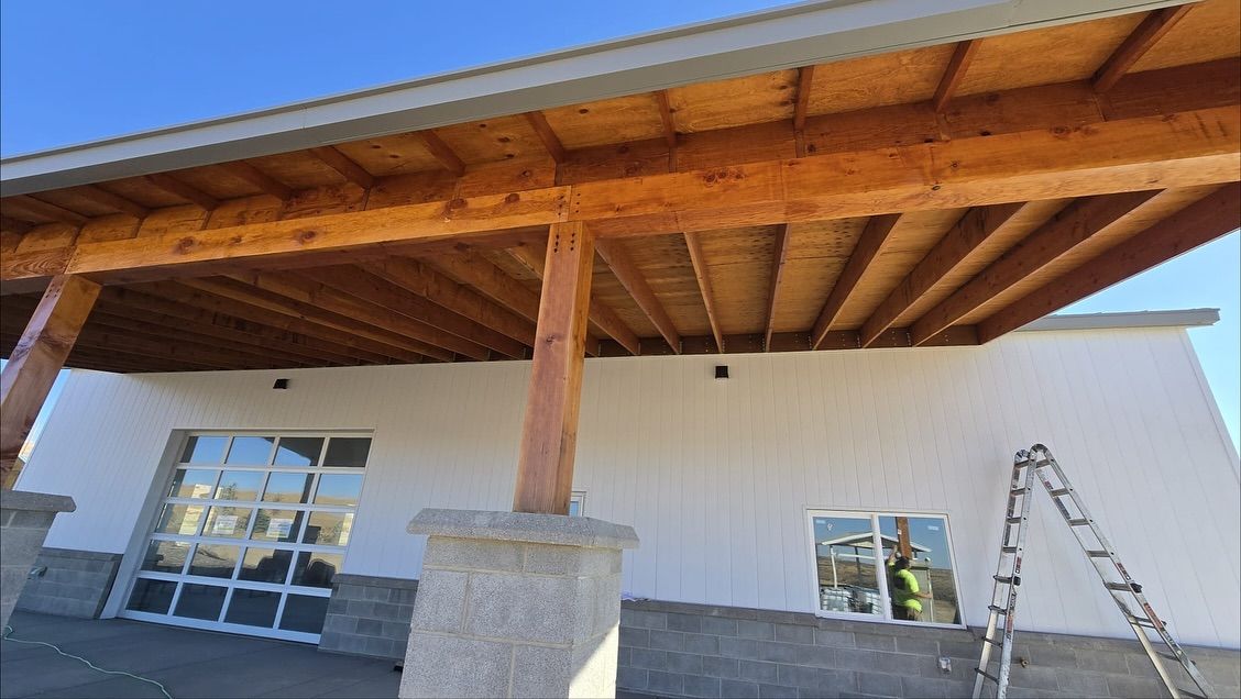 Wooden awning supported by pillars over a building with a glass door and window. Ladder leaning on the wall.