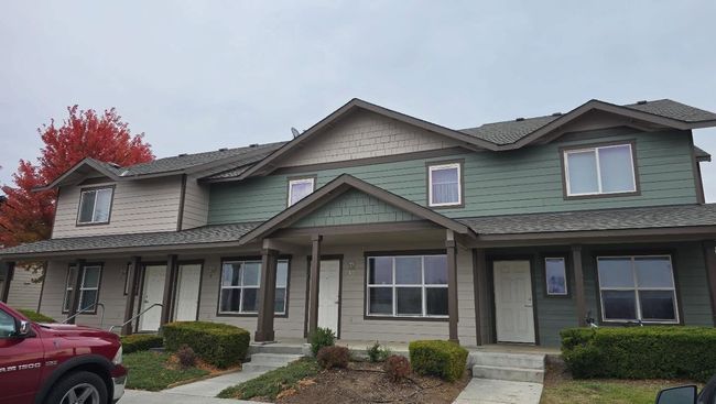 Townhouses with tan and green siding under a cloudy sky, red car in foreground.
