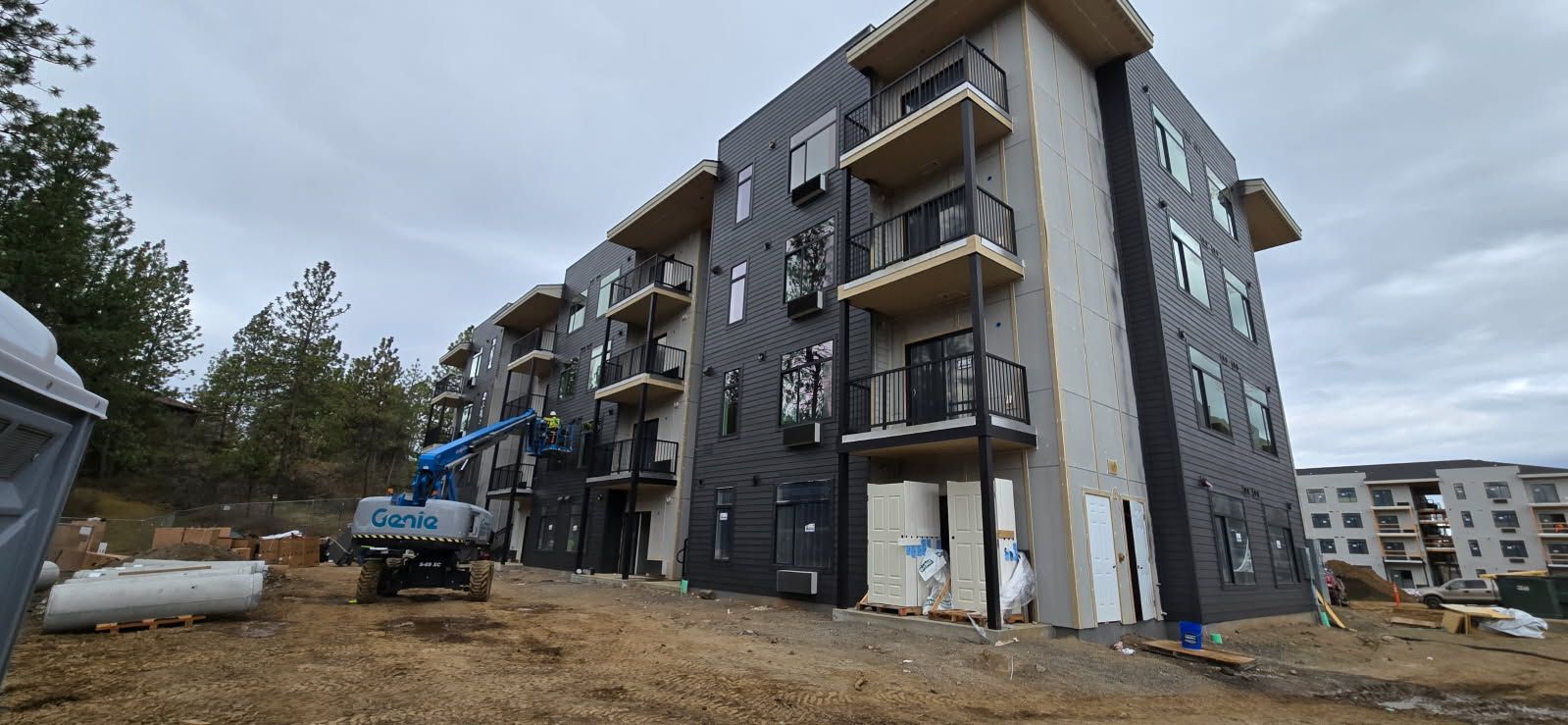 Building under construction; gray siding, balconies, blue lift, and cloudy sky.