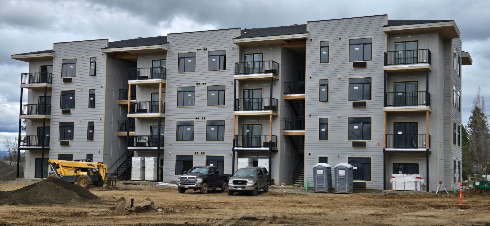 Multi-story apartment building under construction on a dirt lot; construction equipment and porta-potties visible.
