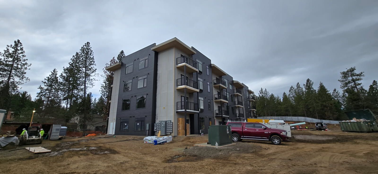 A multi-story building under construction with a cloudy sky. Workers and equipment are on site.