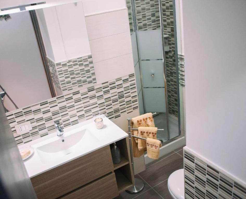 Piccolo bagno con lavabo, specchio, box doccia in vetro e asciugamani a parete in tonalità neutre.