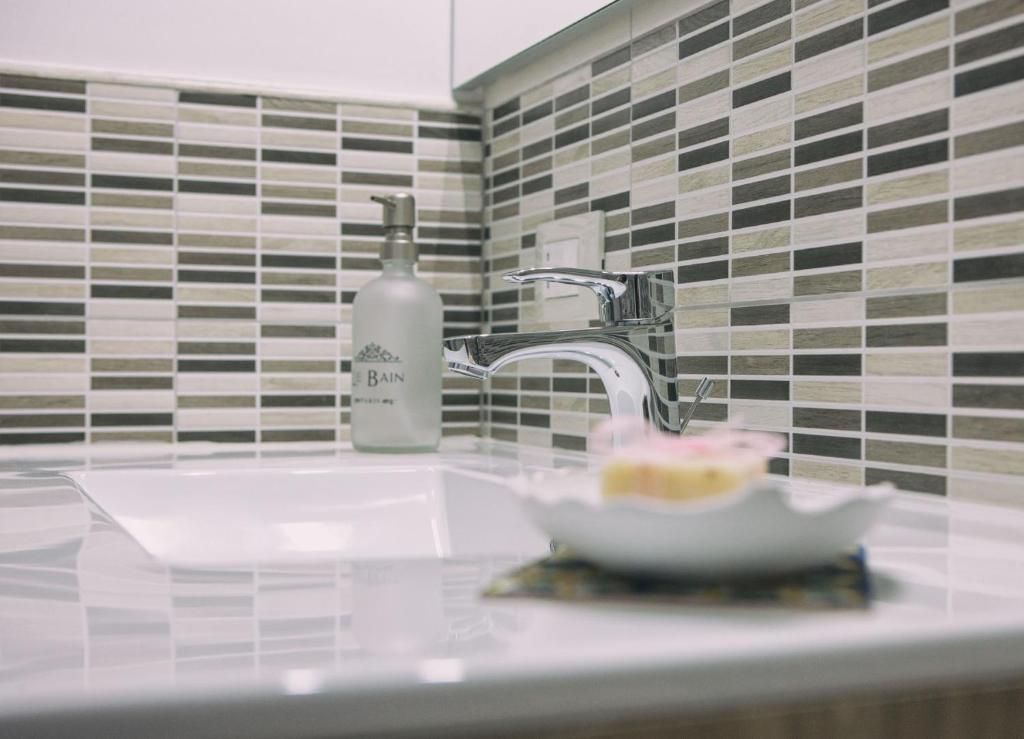 Lavabo del bagno con rivestimento piastrellato, dispenser di sapone, rubinetto e una saponetta sfocata in primo piano.