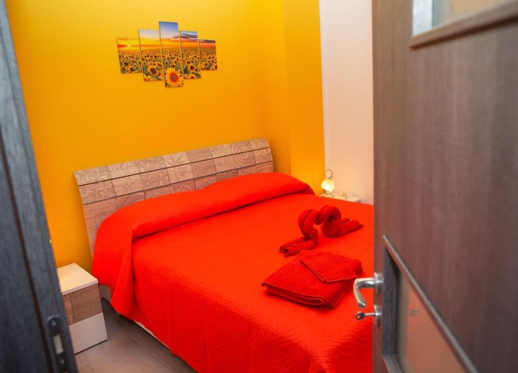 Piccola camera da letto con copriletto rosso, parete arancione e decorazioni murali, vista attraverso una porta aperta.
