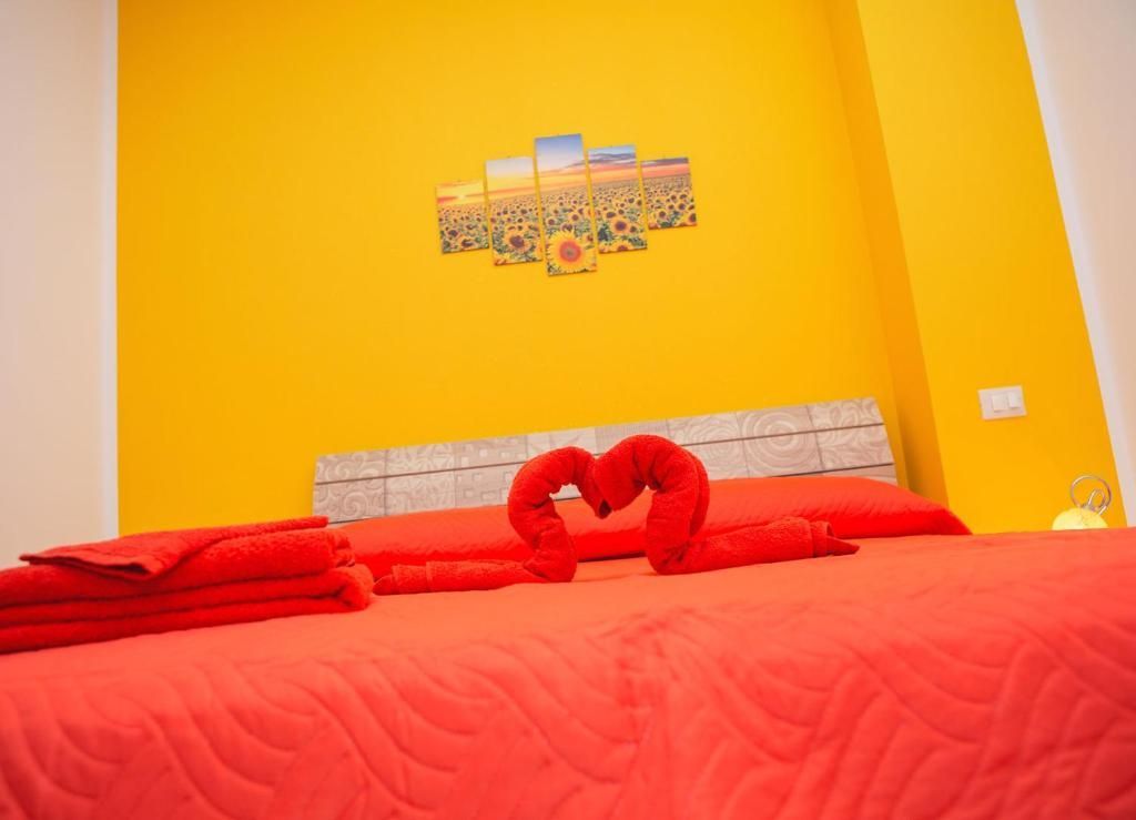 Camera da letto giallo brillante con copriletto rosso e decorazione a forma di cuore realizzata con asciugamani sulla testiera.