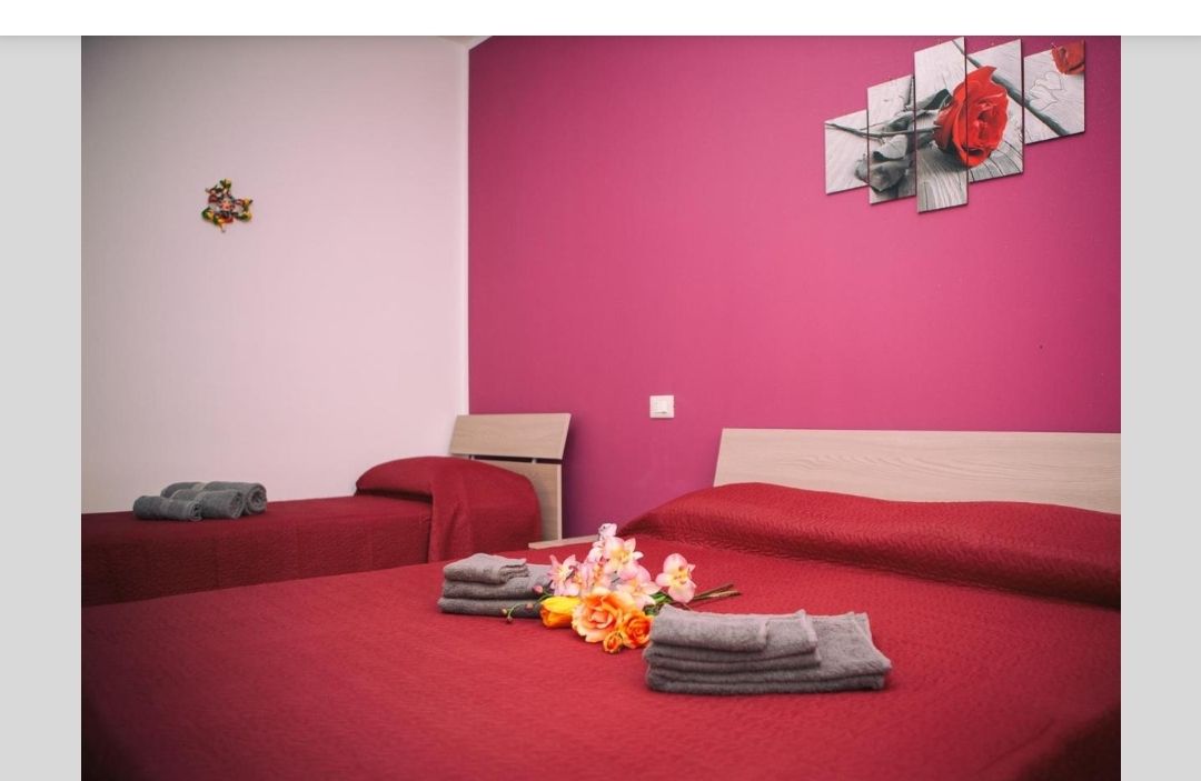 Camera da letto rosa e bianca con copriletto rosso, asciugamani piegati e decorazioni murali.