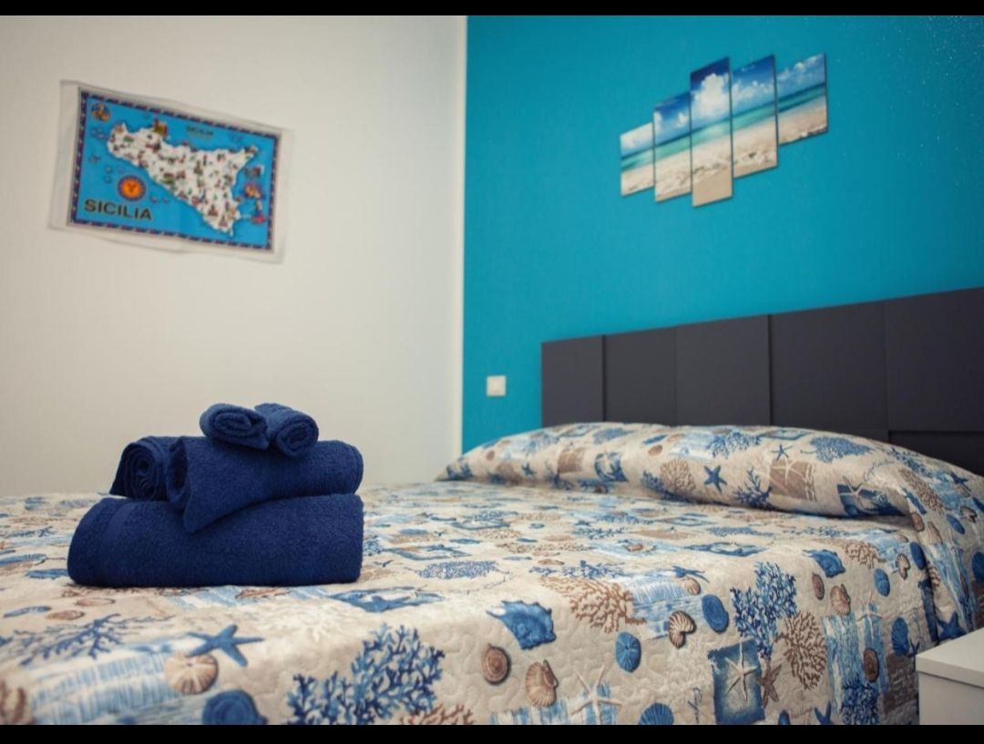 Camera da letto a tema blu con letto ben rifatto, asciugamani piegati e un quadro sopra la testiera.