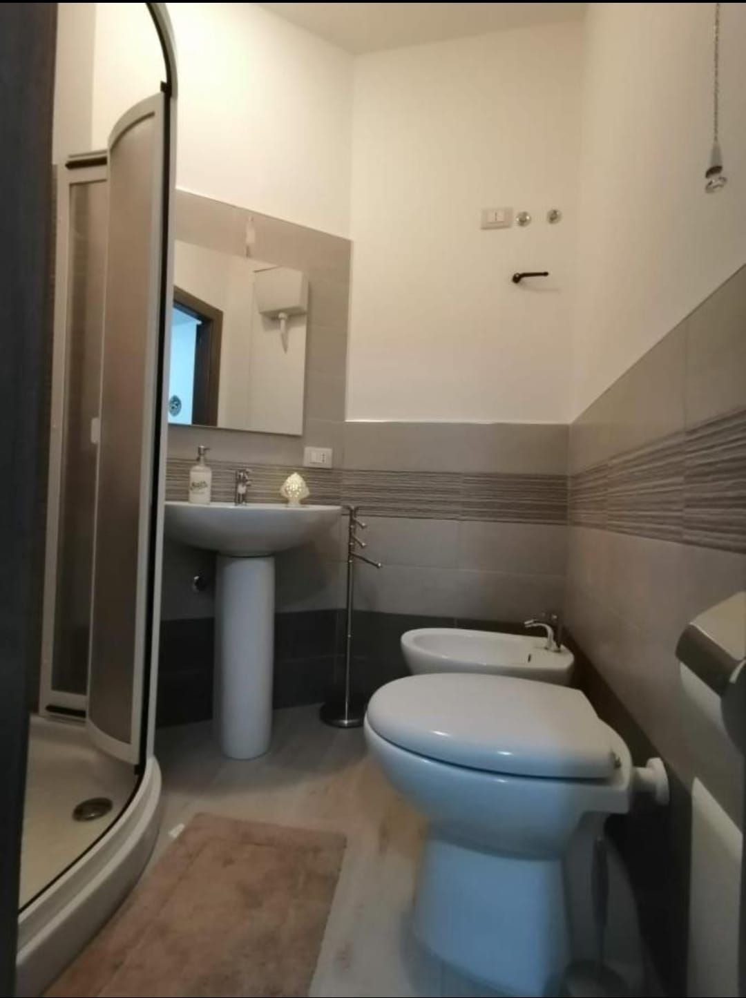 Bagno moderno con doccia, lavabo, WC e bidet in tonalità di grigio chiaro.