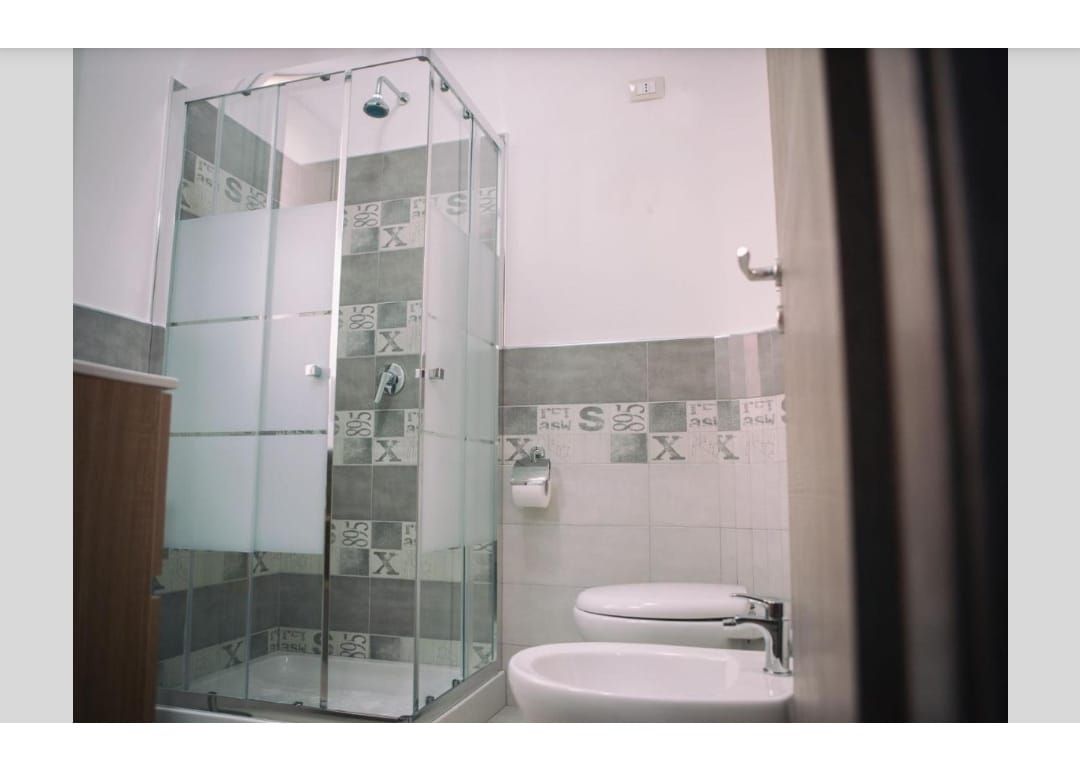 Bagno moderno con box doccia in vetro e WC, piastrellato in bianco e grigio.
