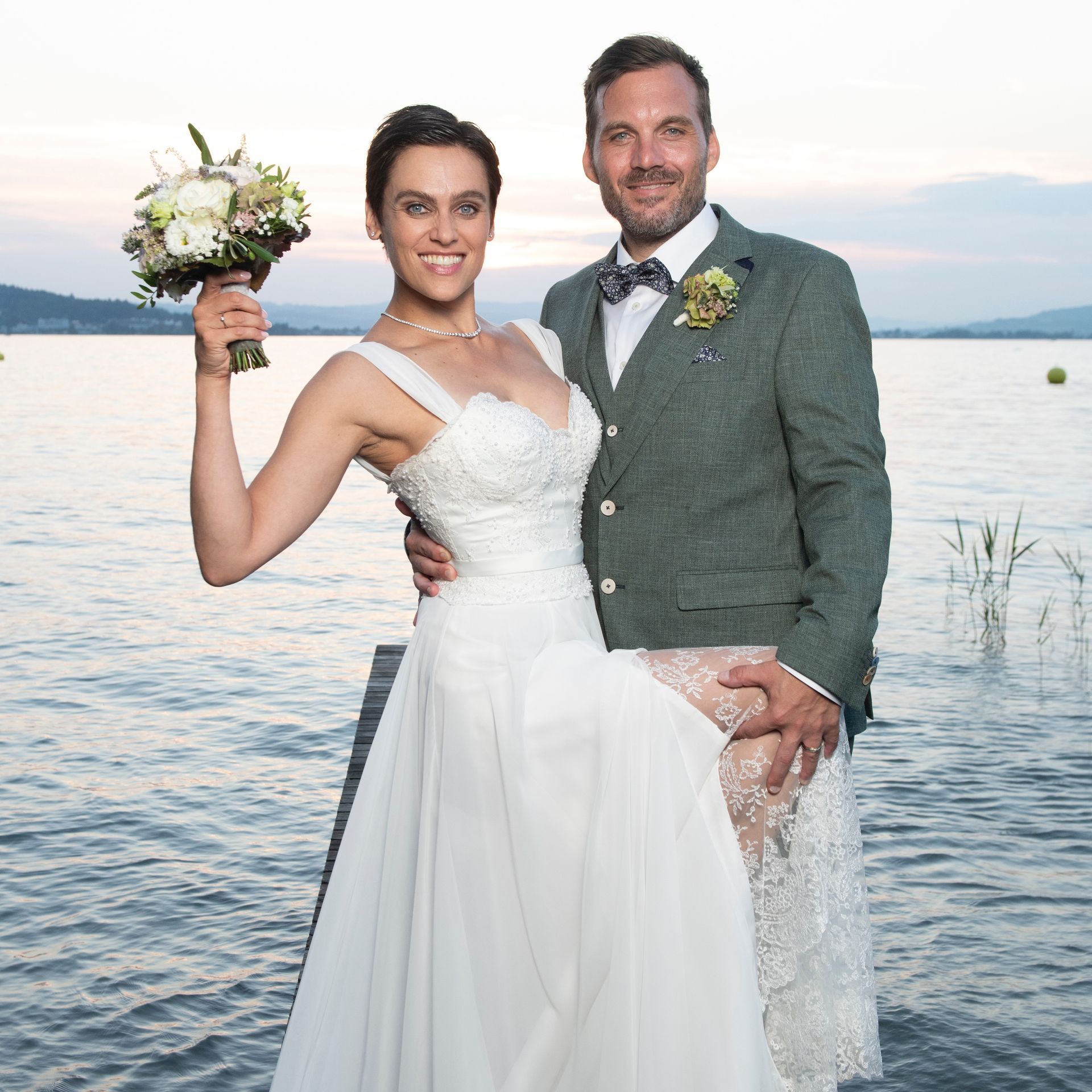 A bride and groom are posing for a picture in front of a body of water.