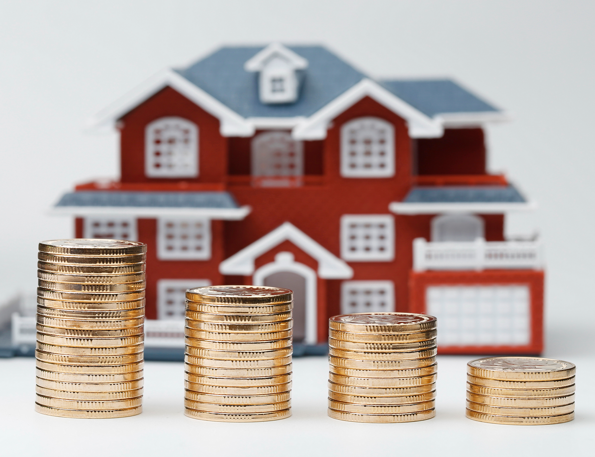 four stacks of gold coins are lined up in front of a model house .