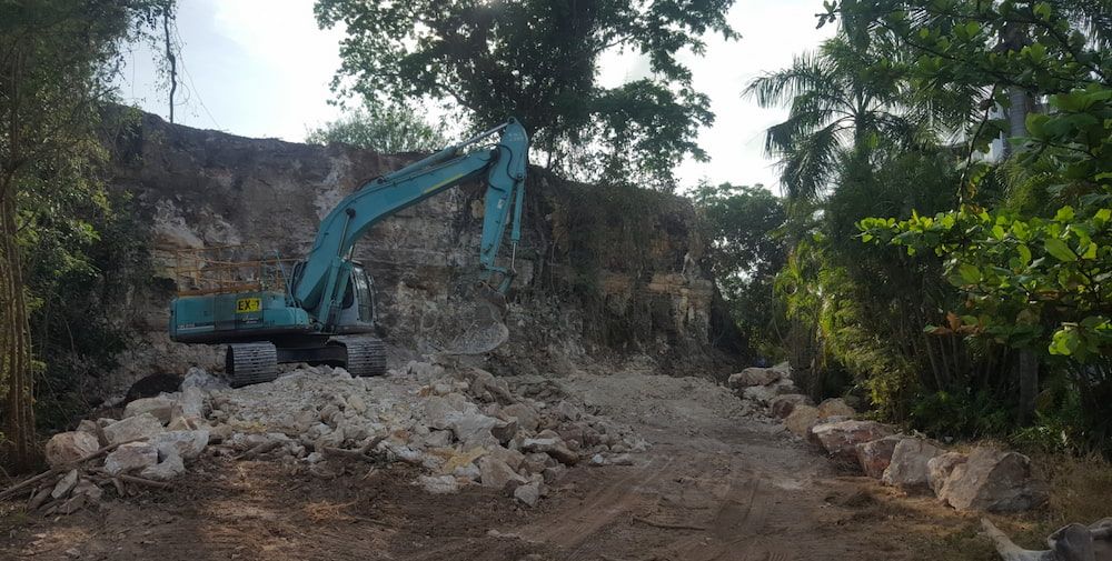 A Blue Excavator is Moving Rocks on a Dirt Road — Diggamen Civil Contracting in Tivendale, NT