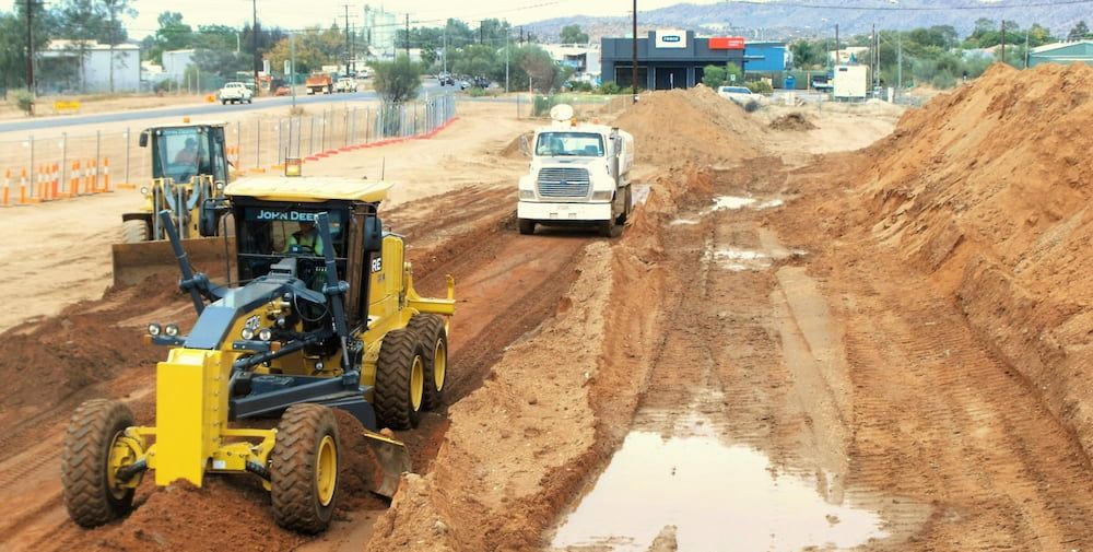 A Yellow Tractor is Driving Down a Dirt Road Next to a White Truck — Diggamen Civil Contracting in Tivendale, NT