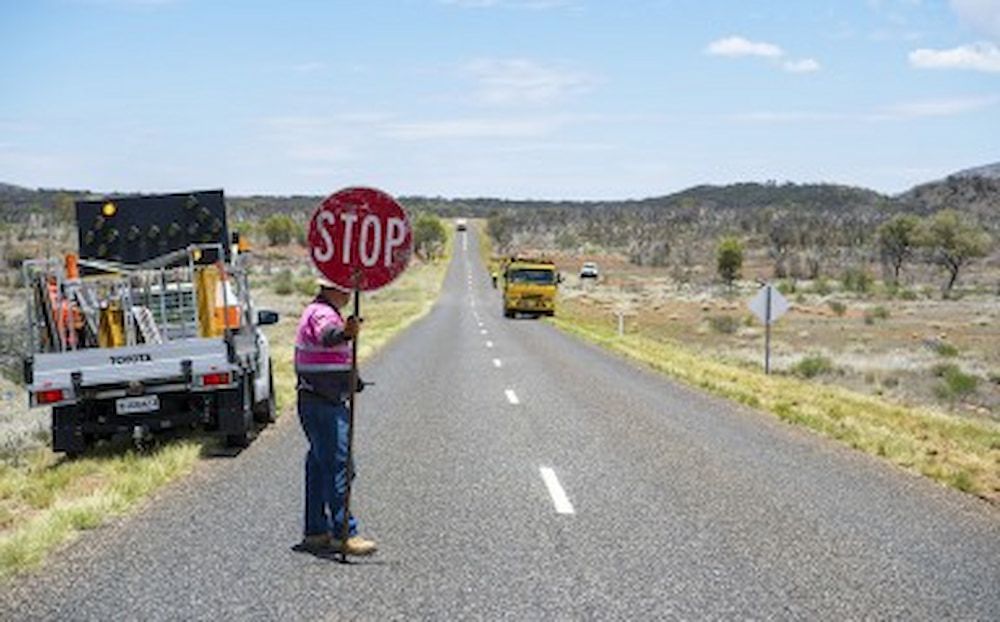 A Man Standing Next to the Street Holding With a Stop Sign — Diggamen Civil Contracting in Tivendale, NT