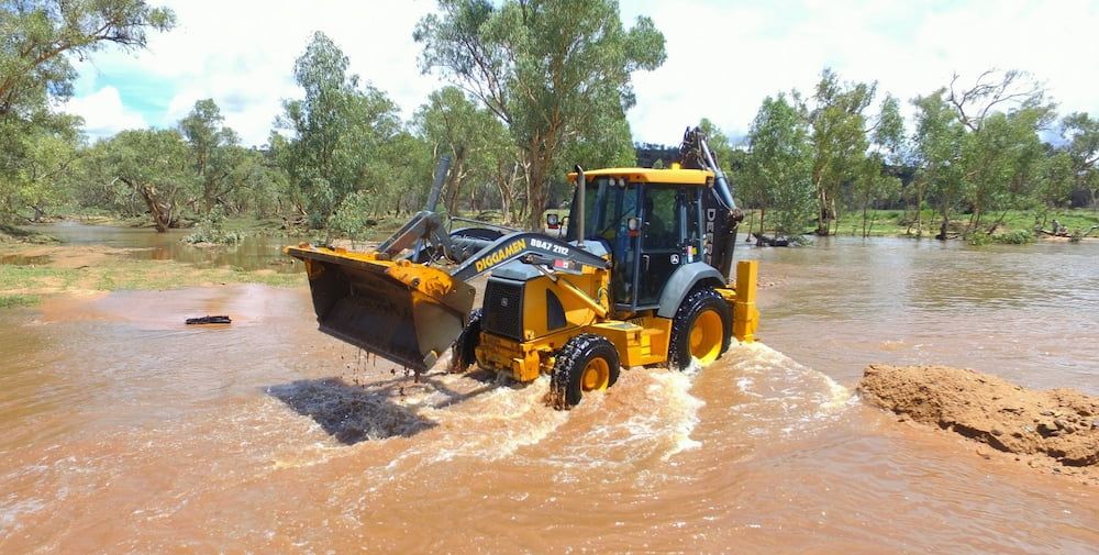 A Yellow Tractor is Driving Through a Flooded Area — Diggamen Civil Contracting in Tivendale, NT