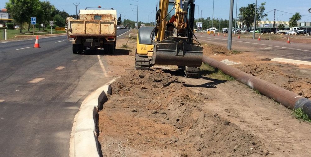A Yellow Excavator is Digging in the Dirt Next to a Dump Truck — Diggamen Civil Contracting in Tivendale, NT
