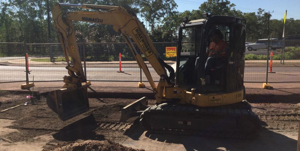 A Man Is Driving a Yellow Excavator on A Construction Site — Diggamen Civil Contracting in Tennant Creek, NT