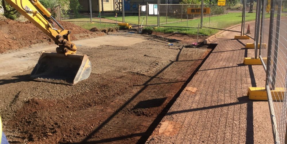 A Yellow Excavator is Working on a Dirt Road Next to a Fence — Diggamen Civil Contracting in Tivendale, NT